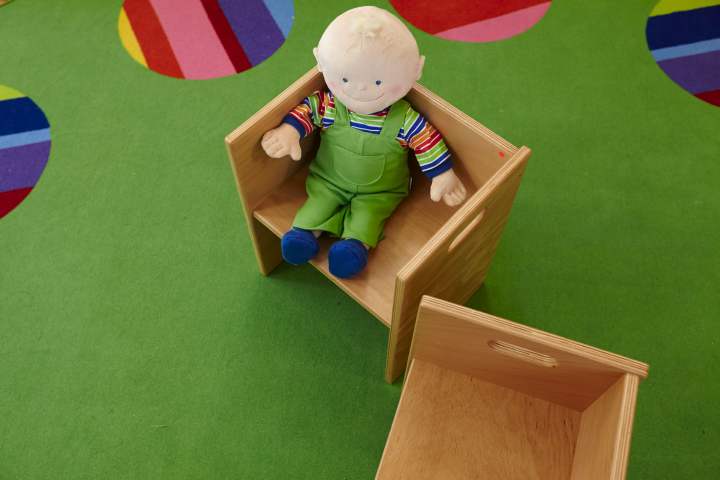 Puppe in einem kleinen Holzstuhl auf einem grünen Spielteppich